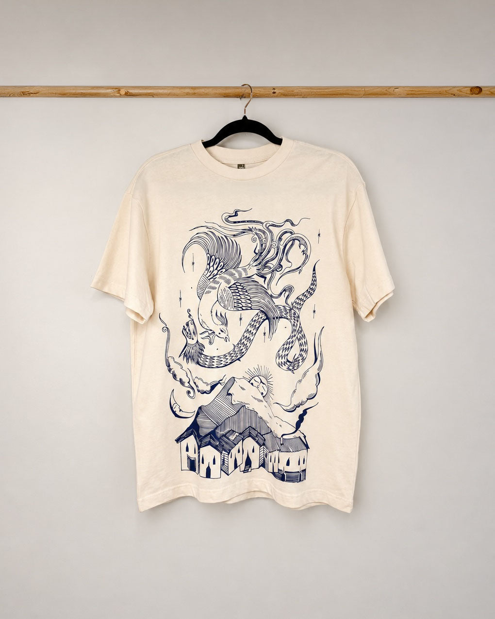 An oversized vintage white box tee featuring an original design by Mexico City-based artist Dariush Ghaderi. A full-front navy blue print bringing together the Simorgh and Quetzalcoatl — mythological deities from Iran and Mexico — in a meditation on wisdom, rebirth, and the unity of sky and earth.